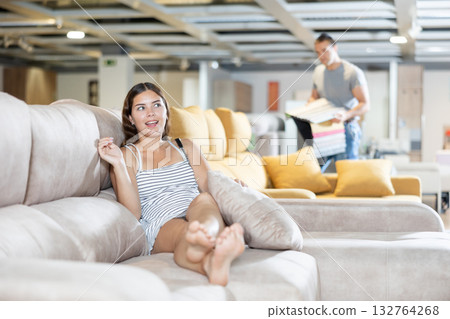 In furniture store,young girl is sitting on sofa with ottoman 132764268