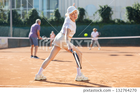 Sporty aged family during doubles match on tennis court. Active lady hitting tennis ball with racket 132764270