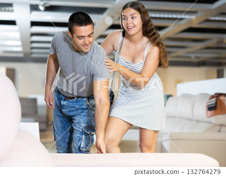 Newlyweds choose upholstered furniture in store and carefully feel cotton covering of seat 132764279