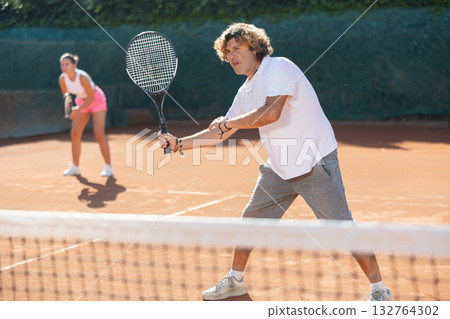 Couple of young paddle tennis players enjoying double match. Positive man training serving ball Couple of young paddle tennis players enjoying double match. Positive man training serving ball 132764302