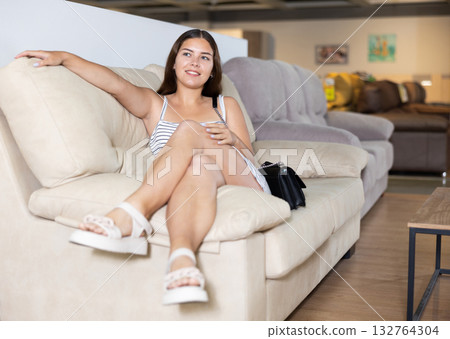 In furniture store,young girl is sitting on sofa with ottoman 132764304