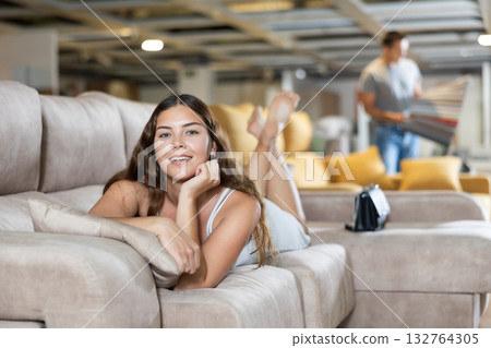 On sofa girl is lying on stomach with chin propped up in hands in furniture store 132764305