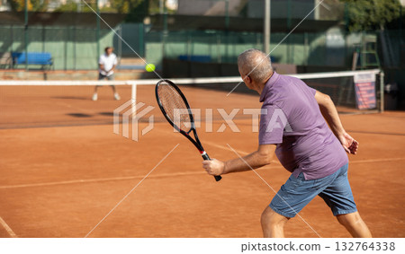 Rear view of focused european aged man playing tennis match in court of tennis club 132764338