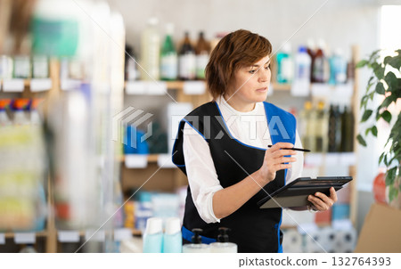 Woman seller, with tablet in hands, make inventory in store. 132764393