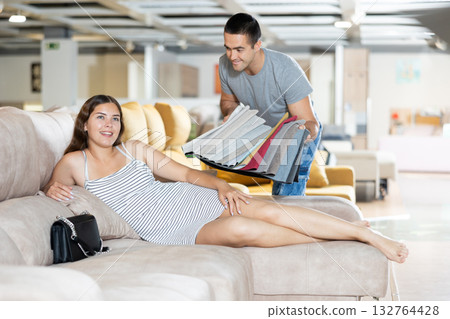 Woman is sitting on sofa and sales consultant shows her set of upholstery fabrics 132764428