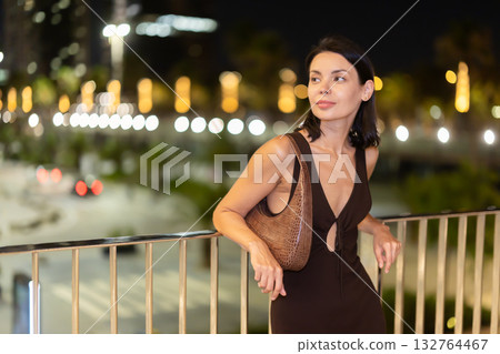 Young woman leaning on metal railing against background of blurred city lights 132764467