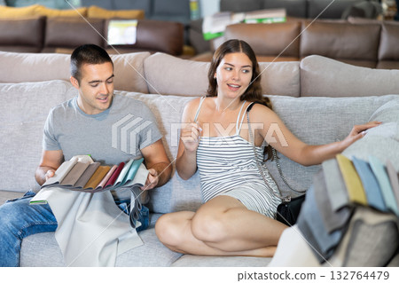 In store wife sit with legs on gray sofa to test in use,husband examines upholstery fabric 132764479
