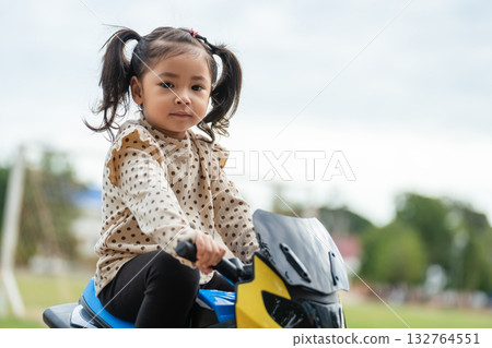 toddler girl riding an electric motorcycle toy in park toddler girl riding an electric motorcycle toy in park 132764551