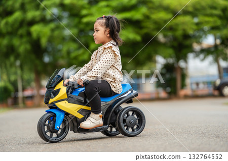toddler girl riding an electric motorcycle toy in park toddler girl riding an electric motorcycle toy in park 132764552