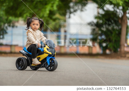 toddler girl riding an electric motorcycle toy in park toddler girl riding an electric motorcycle toy in park 132764553
