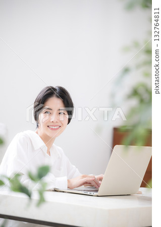 畫面中一位女性家庭主婦或設計師正在家中遠距辦公，房間裡擺放著綠植，她正在使用電腦。 132764811