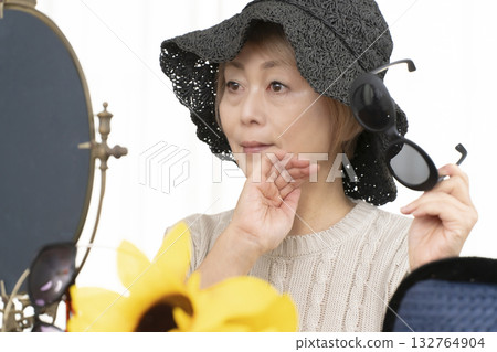 Senior women choosing hats and sunglasses to protect themselves from UV rays when going out in the summer Senior women choosing hats and sunglasses to protect themselves from UV rays when going out in the summer 132764904