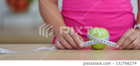 Healthy Lifestyle. Woman measuring apple with tape, promoting health awareness and nutrition. 132766274