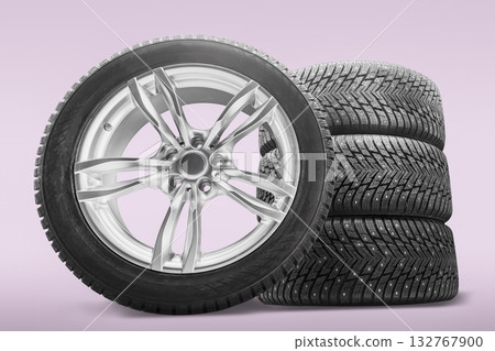 A tire shop showcases a set of four winter tires stacked beside an alloy wheel. These studded tires are designed for improved traction in winter conditions, perfect for safe driving. A tire shop showcases a set of four winter tires stacked beside an alloy wheel. These studded tires are designed for improved traction in winter conditions, perfect for safe driving. 132767900