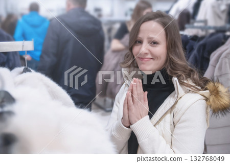 A 30-35-year-old white woman with a smile and pleading looks dreamily at her friend into the camera in a fashion boutique - she dreams of a new fur coat and asks to be given a white coat for Christmas A 30-35-year-old white woman with a smile and pleading looks dreamily at her friend into the camera in a fashion boutique - she dreams of a new fur coat and asks to be given a white coat for Christmas 132768049