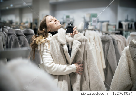 A beautiful 30-35-year-old woman dreamily hugs a new winter fur coat in a fashion boutique store. She dreams of giving a gift or buying a new fashionable fur coat or winter coat. A beautiful 30-35-year-old woman dreamily hugs a new winter fur coat in a fashion boutique store. She dreams of giving a gift or buying a new fashionable fur coat or winter coat. 132768054