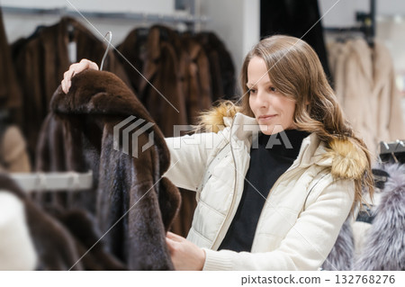 A white young beautiful woman of 30-35 years old is looking at an expensive mink fur coat in a fashionable clothing boutique. Seasonal winter fashion shopping and women's Christmas holiday shopping A white young beautiful woman of 30-35 years old is looking at an expensive mink fur coat in a fashionable clothing boutique. Seasonal winter fashion shopping and women's Christmas holiday shopping 132768276