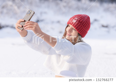 Young woman in a red hat takes a selfie in a snowy landscape during a bright winter day Young woman in a red hat takes a selfie in a snowy landscape during a bright winter day 132768277