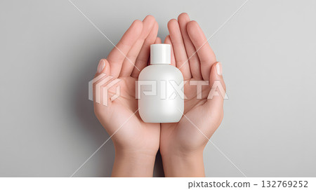 Hands holding a white cosmetic bottle on a soft gray background for beauty product display Hands holding a white cosmetic bottle on a soft gray background for beauty product display 132769252