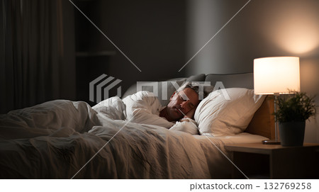 Man sleeping peacefully in a cozy bedroom with soft lighting and warm atmosphere 132769258