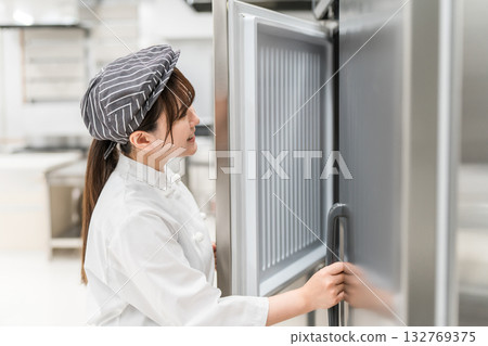 A woman chef in a chef's coat taking ingredients out of the refrigerator A woman chef in a chef's coat taking ingredients out of the refrigerator 132769375