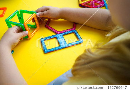 A colorful collection of magnetic geometric shapes is being transformed by a child into creative three-dimensional designs and constructions. 132769647