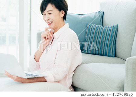 A middle-aged woman operating a computer in the living room 132769850