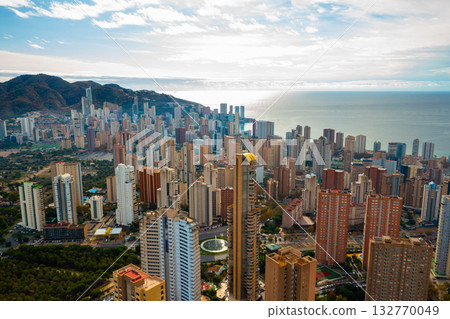 Scenic panoramic view of Benidorm with numerous skyscrapers rising above the coastline. Mediterranean resort city on Costa Blanca, Alicante, Spain. Clear sunny day with blue sky and sea. 132770049