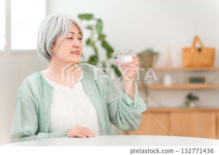 一位白髮老年婦女在家裡的客廳喝著礦泉水 132771436