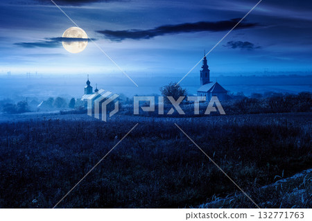 old church in the village in autumn at night. view of countryside landscape from a hill in haze and full moon light. empty rural fields. background for investment or abstract concepts 132771763