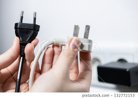 Hands comparing black European and white British electrical plugs, illustrating global power compatibility standards for international travel and device connectivity solutions 132772153