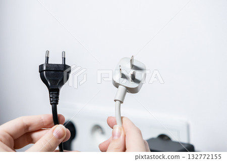 Person holding diverse electrical plugs, European and UK types, illustrating international power compatibility and adapter needs for travel 132772155