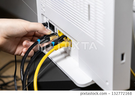 Adult hand firmly inserting a crucial black Ethernet LAN network cable into a modern white Wi-Fi router, enabling swift internet connectivity and robust digital network access 132772168