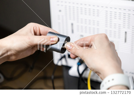 Person's hands meticulously connect an Ethernet LAN cable into a sleek gray adapter, ensuring stable internet for digital work and home office connectivity 132772170