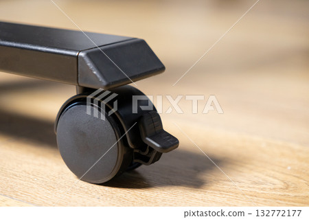 Black furniture caster wheel featuring a locking mechanism on a light wooden floor, promoting mobility and stability for modern office or home furnishings Black furniture caster wheel featuring a locking mechanism on a light wooden floor, promoting mobility and stability for modern office or home furnishings 132772177