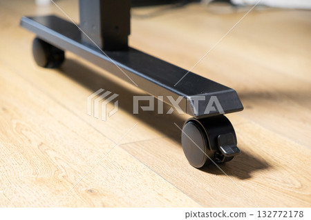 Black caster wheel with a lock on a modern furniture base, offering mobility and stability for adjustable desks in a home office environment 132772178