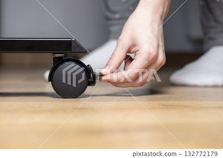 Person's hand adjusting a black caster wheel brake on a furniture leg, ensuring stability and safety for home furniture assembly or renovation Person's hand adjusting a black caster wheel brake on a furniture leg, ensuring stability and safety for home furniture assembly or renovation 132772179