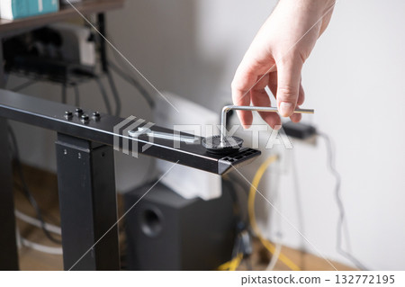 Person's hand expertly using an Allen wrench to securely fasten a screw into a black metal desk frame, symbolizing practical home assembly and DIY project skills Person's hand expertly using an Allen wrench to securely fasten a screw into a black metal desk frame, symbolizing practical home assembly and DIY project skills 132772195