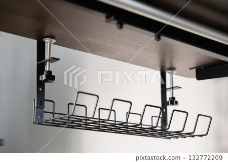 Black wire cable management tray securely clamped beneath a modern dark wooden desk, promoting an organized, tidy, and productive home office environment Black wire cable management tray securely clamped beneath a modern dark wooden desk, promoting an organized, tidy, and productive home office environment 132772209