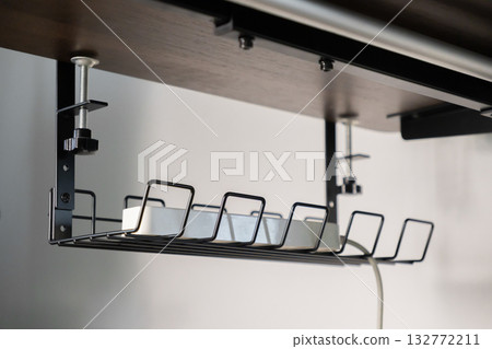 Modern under-desk cable management tray securely holding a white power strip, promoting a tidy professional workspace and efficient home office organization Modern under-desk cable management tray securely holding a white power strip, promoting a tidy professional workspace and efficient home office organization 132772211