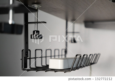 Durable black metal wire cable management tray securely clamped under dark wooden office desk, neatly organizing essential power strip for optimal productive home workspace Durable black metal wire cable management tray securely clamped under dark wooden office desk, neatly organizing essential power strip for optimal productive home workspace 132772212