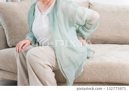 一位老年婦女因背痛而坐在客廳沙發上。 132773971