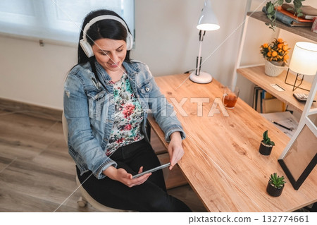 Freelancer working from home listening music with headphones and holding tablet Freelancer working from home listening music with headphones and holding tablet 132774661
