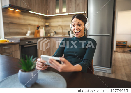 Very happy young girl with white headphones enjoy using a mobile phone indoor 132774685