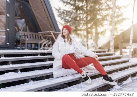 Young woman in cozy winter outfit enjoys the snowy terrace at a mountain cabin during a sunny afternoon 132775487