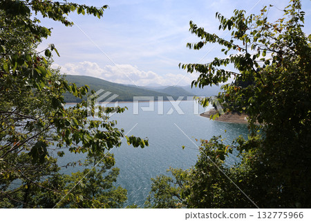 Scenic lake view surrounded by trees on a sunny day in a mountainous landscape Scenic lake view surrounded by trees on a sunny day in a mountainous landscape 132775966