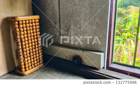 A beaded chair leaning against the wall next to an open sliding window 132775986