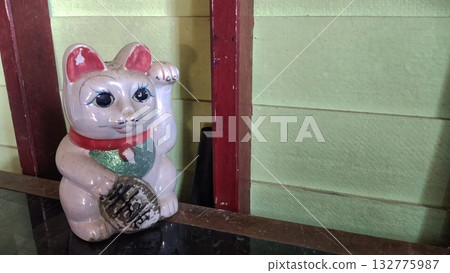 An old lucky cat brings good luck to its owner, placed on the table next to the wall 132775987