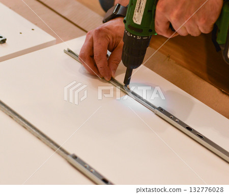 Furniture assembly. A worker is screwing a hinge into a wooden closet door. Adjustment of fittings, door hinges. The concept of installing furniture, home renovation. Furniture assembly. A worker is screwing a hinge into a wooden closet door. Adjustment of fittings, door hinges. The concept of installing furniture, home renovation. 132776028