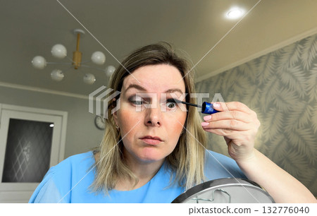 The girl carefully blends eyeshadow, her reflection showing concentration and excitement for her upcoming event. 132776040